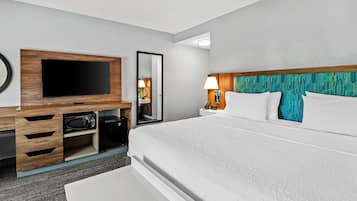 Habitación de hotel con cama, televisión montada en un mueble de madera, mesita de noche con lámpara y espejo.