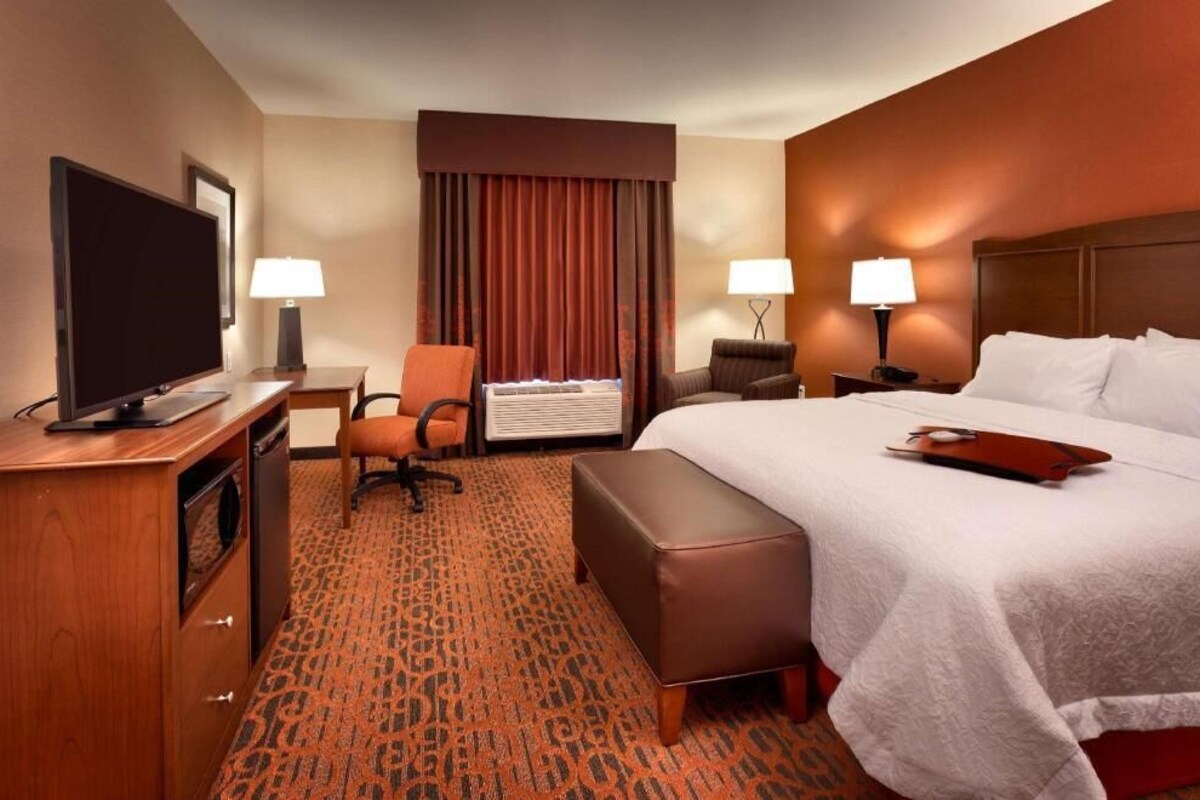 Une chambre d’hôtel comprenant un lit, un bureau avec une télévision, une chaise, un appareil de climatisation et une fenêtre avec des rideaux.