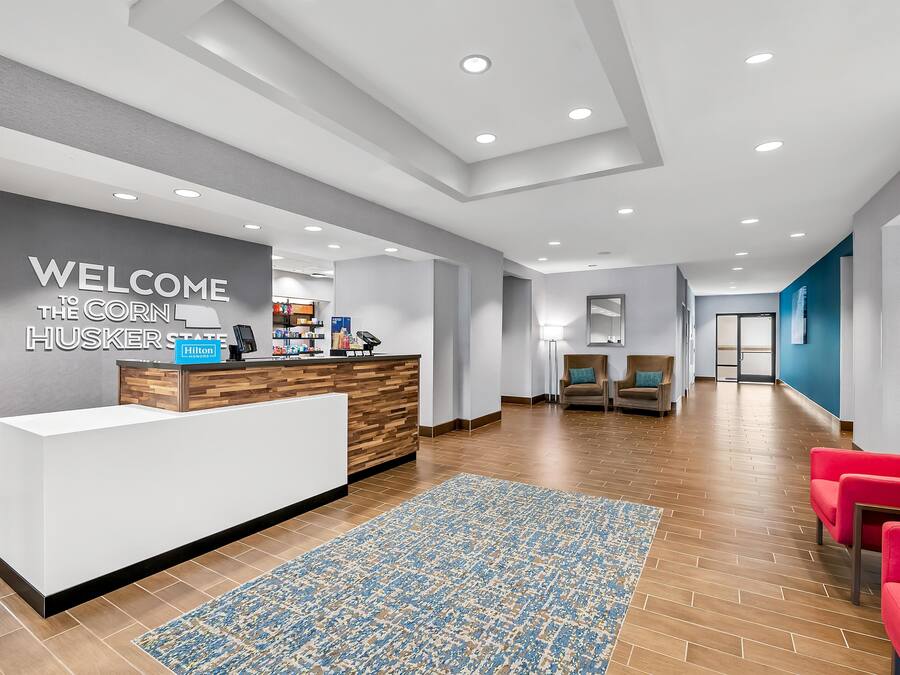 A hotel reception area with a modern design, a reception desk, seating area, and a hallway leading to other rooms.