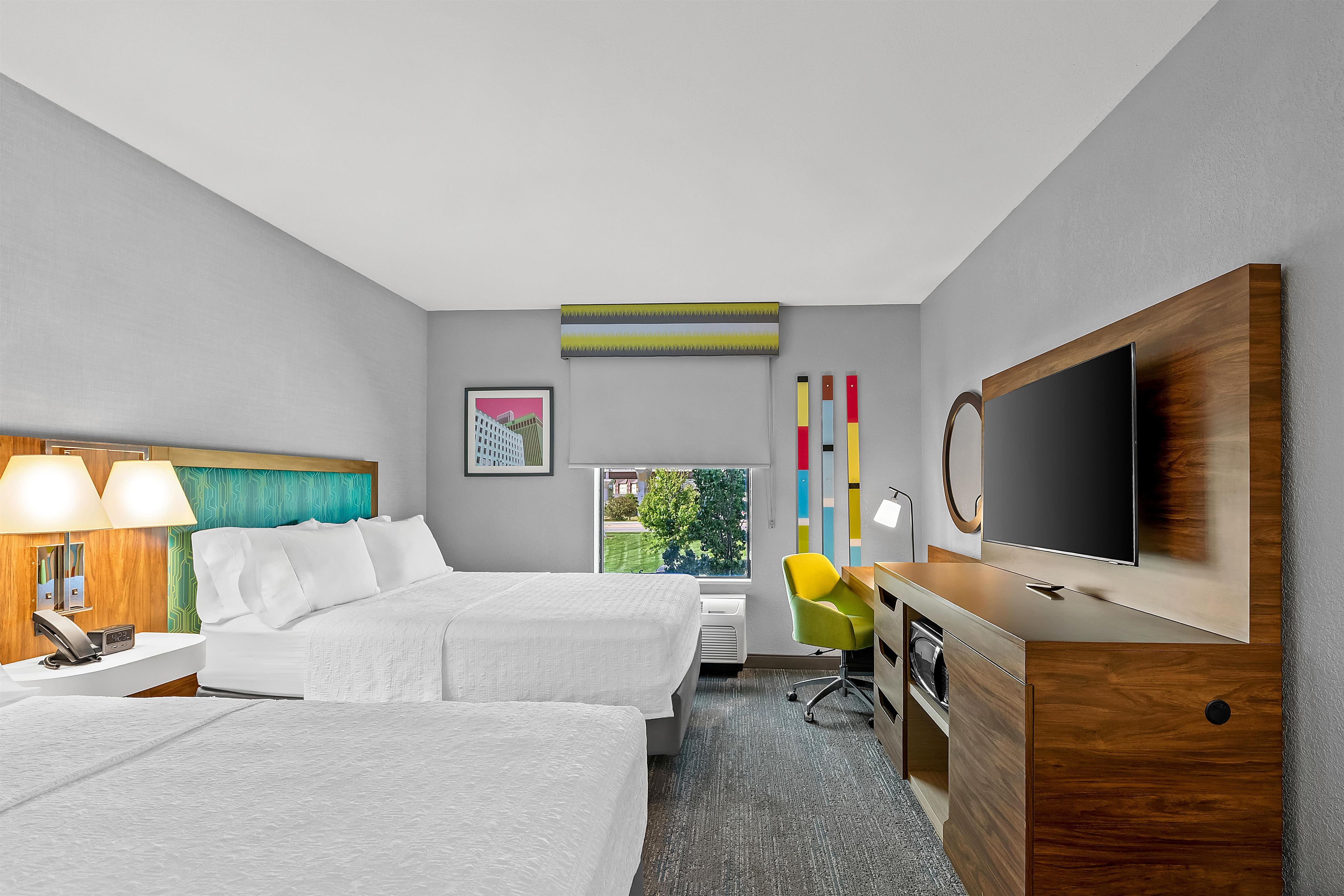 A hotel room with a bed, bedside tables, a desk, a chair, a TV, and a window with a view.