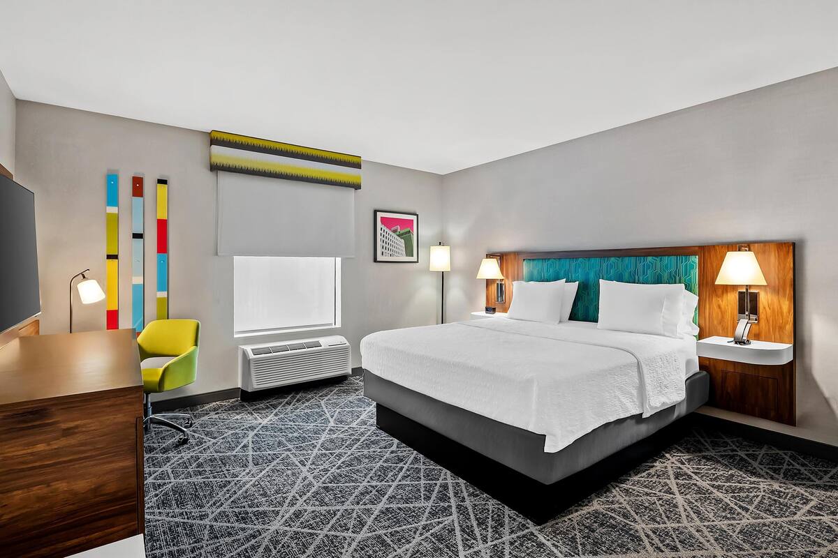 A hotel room with a bed, a desk, a chair, a TV, and a window.