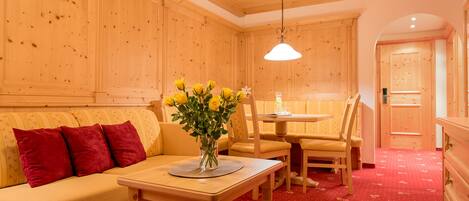 Una habitación acogedora con paredes de madera y alfombra roja, que incluye un sofá, una mesa de comedor con sillas y un jarrón con flores amarillas.