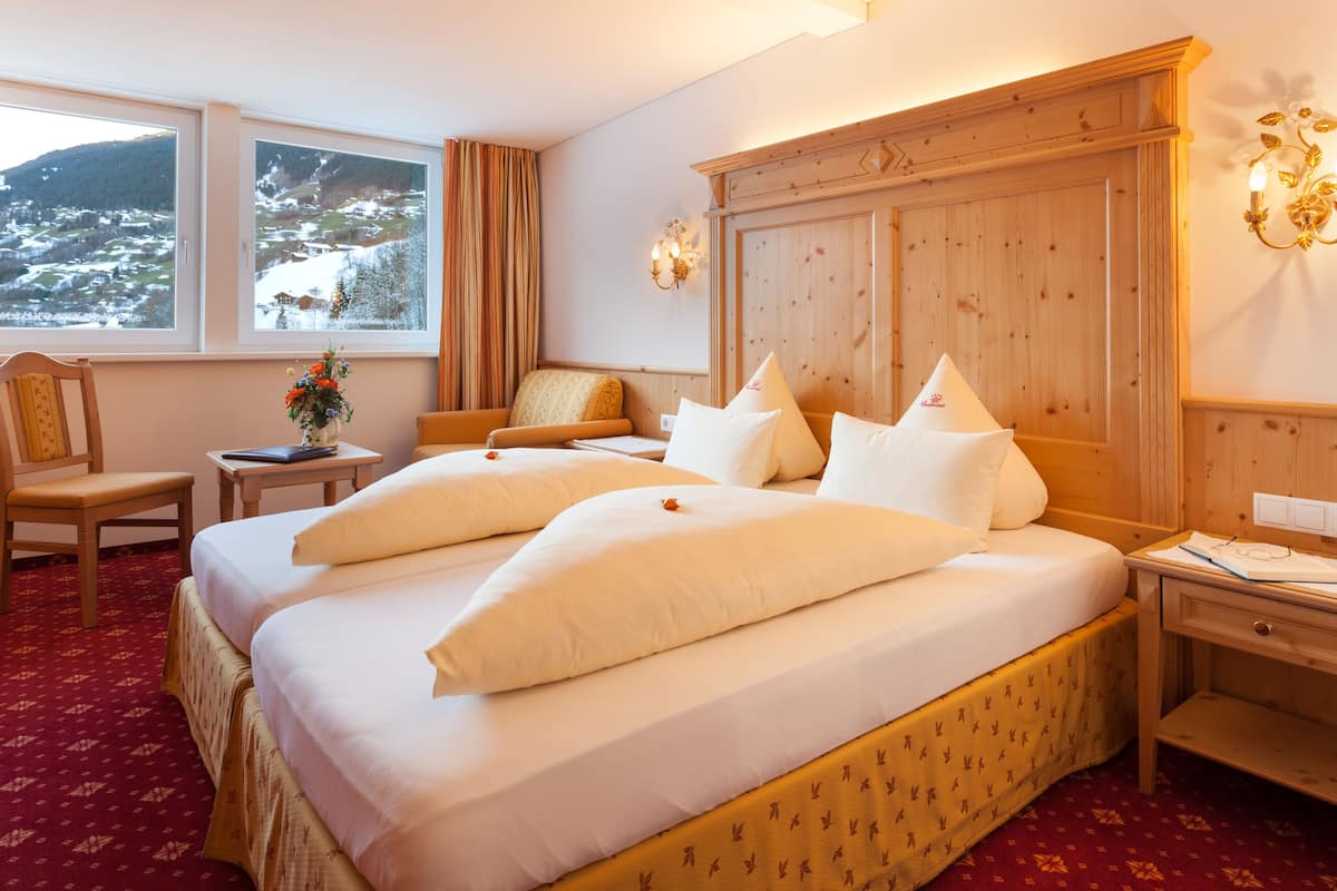 Habitación de hotel con dos camas, cabecero de madera, escritorio, una silla y vistas a un paisaje nevado a través de las ventanas.