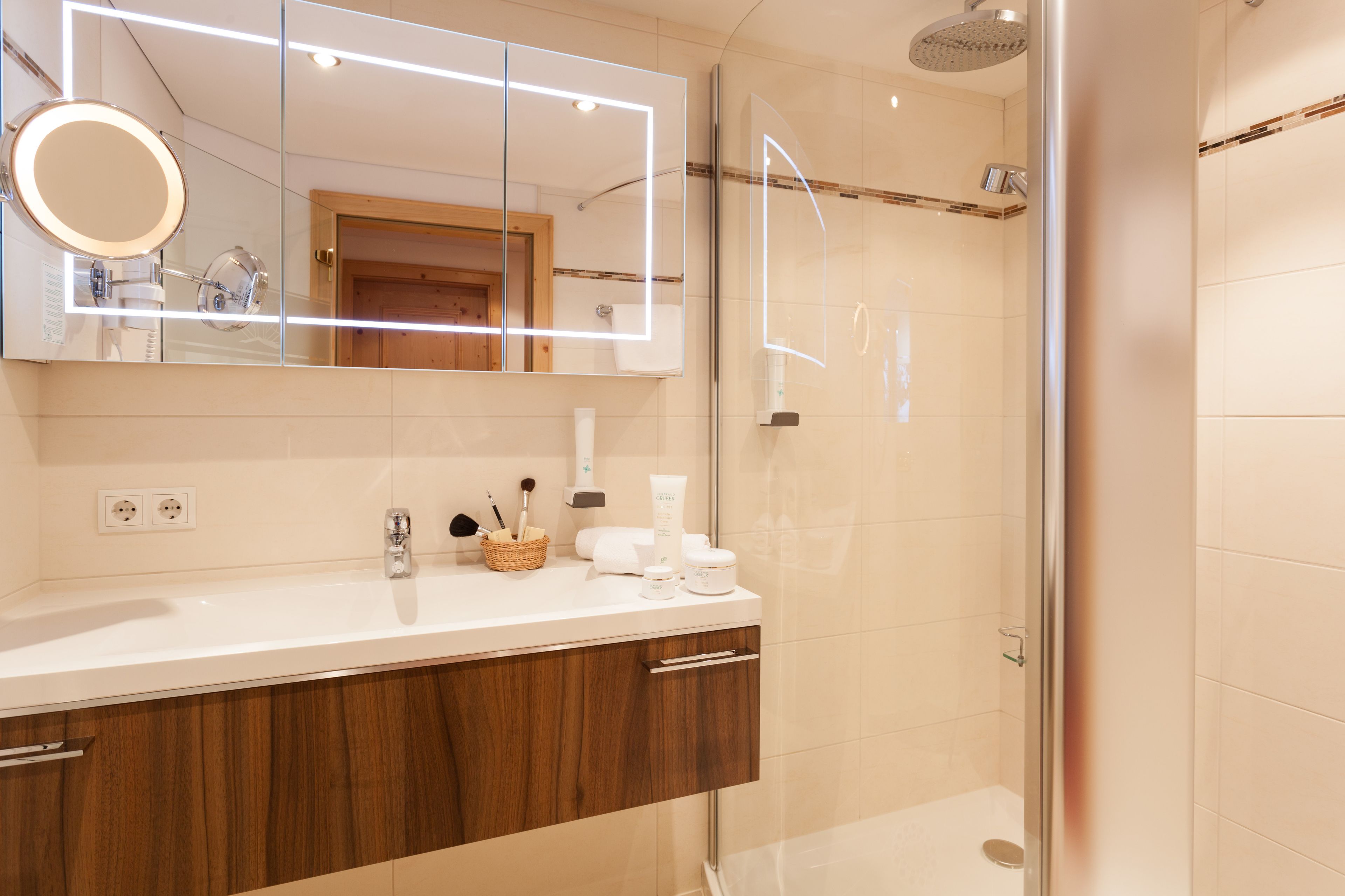 Een moderne badkamer met een grote spiegel, een douche en een wastafel met toiletartikelen.