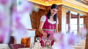 A person in traditional attire setting a table with wine glasses and cutlery. - Hotel Bergkristall (Silbertal)
