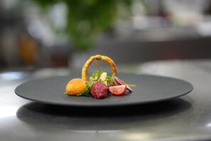 A black plate with a food item, a small round object, and some vegetables. - Hotel Bergkristall (Silbertal)