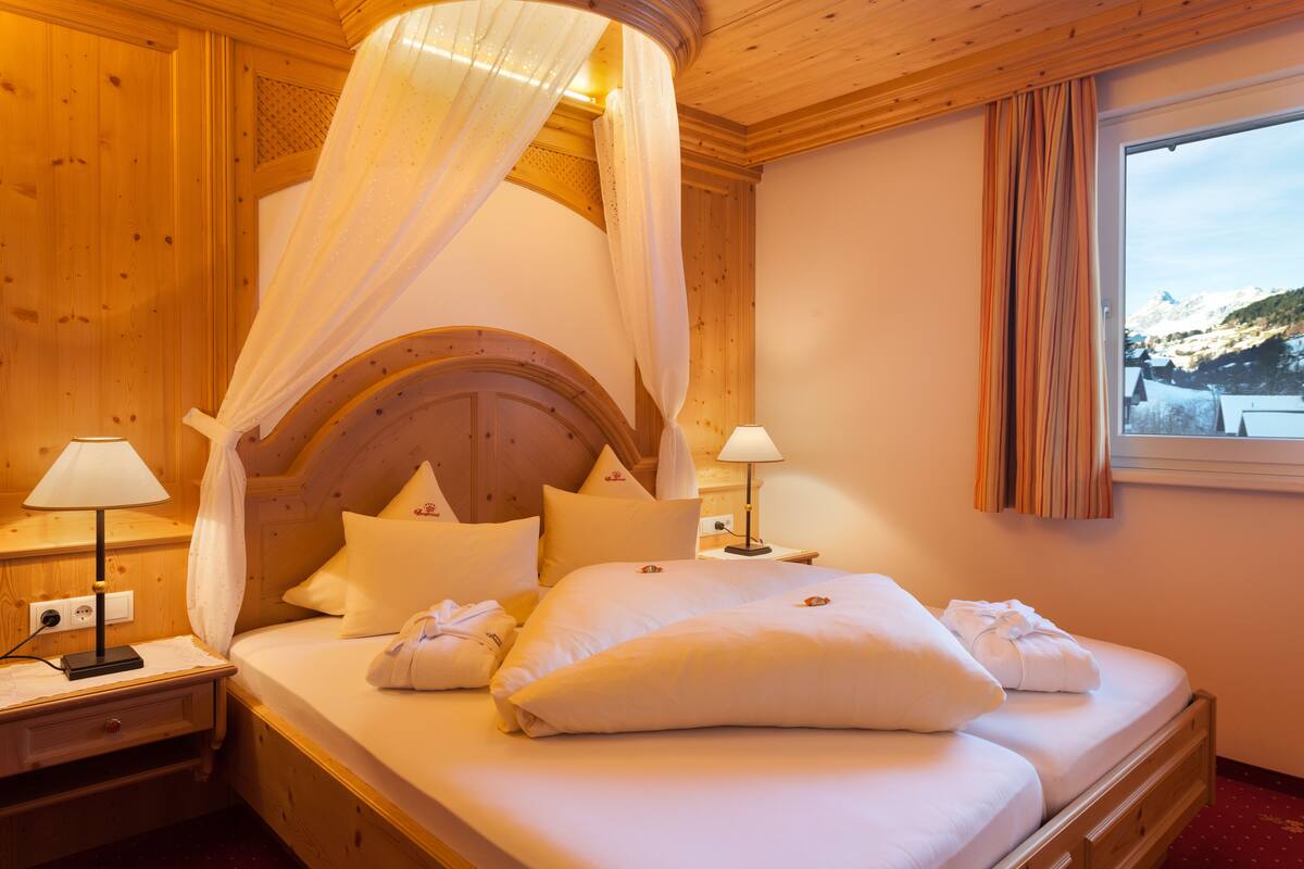 Una habitación de madera con una cama, dos mesitas de noche y un ventanal con cortinas.