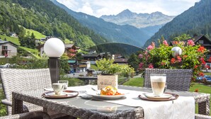 A table set outdoors with a mountain view, a wicker chair, and a table lamp. - Hotel Bergkristall (Silbertal)