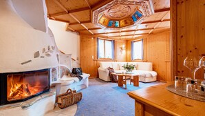A cozy room with a fireplace, a sofa, a table, and a wooden ceiling. - Hotel Bergkristall (Silbertal)