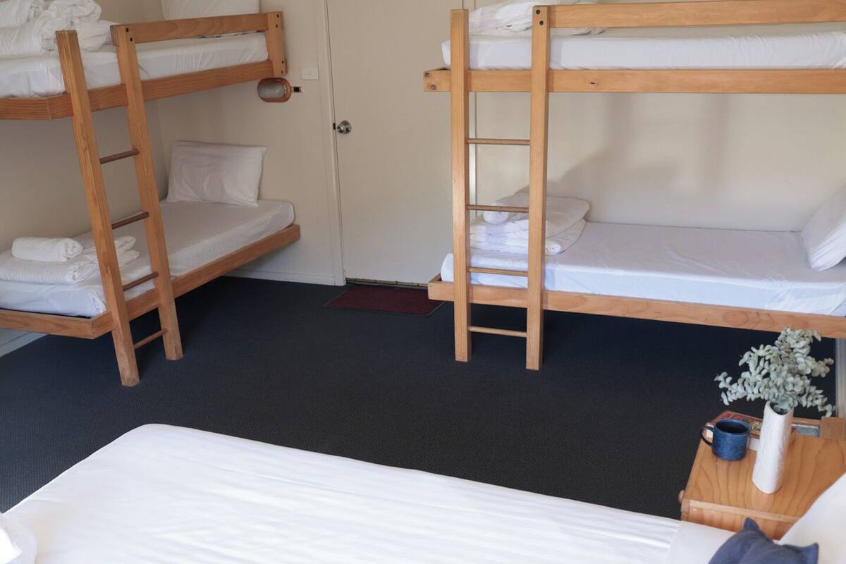 A room with bunk beds, a single bed, a door, and a small table with a vase.