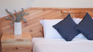 A bed with white and dark gray pillows, a wooden headboard, a bedside table with a drawer, and a white vase with a plant. - Ski Rider Hotel (Wilsons Valley)