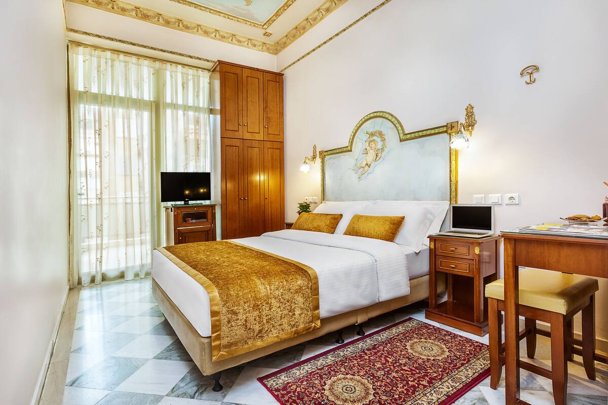 A hotel room with a large bed, wooden wardrobe, desk, and a television.