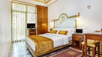 A hotel room with a large bed, wooden wardrobe, desk, and a television.