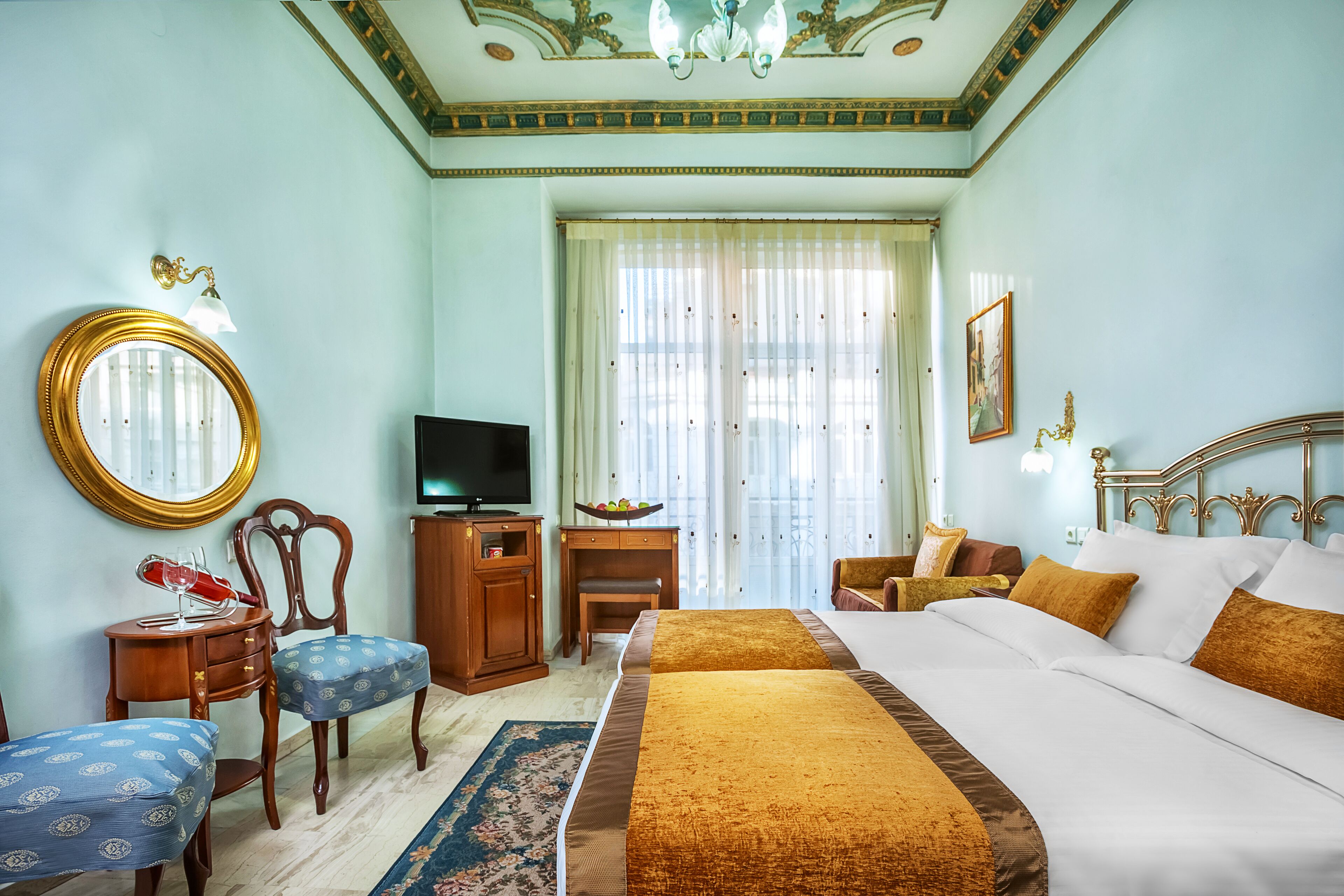 A hotel room with a large bed, a television, a desk with a chair, a round mirror, and a window with curtains.