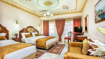 A hotel room with two beds, a desk with a computer, a TV, and a large window with curtains.