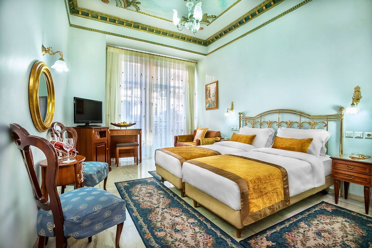 A spacious bedroom with a large bed, a desk, a chair, and a television.