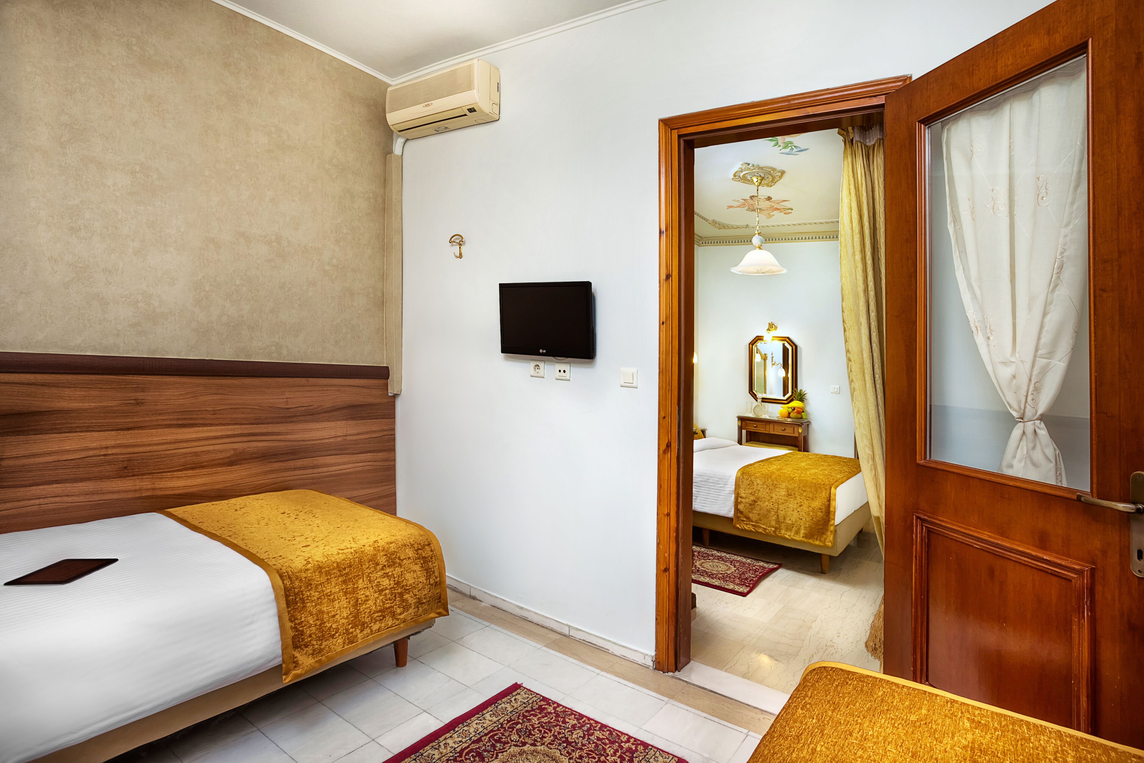 A hotel room with two beds, a TV, a wooden door, and a mirror.