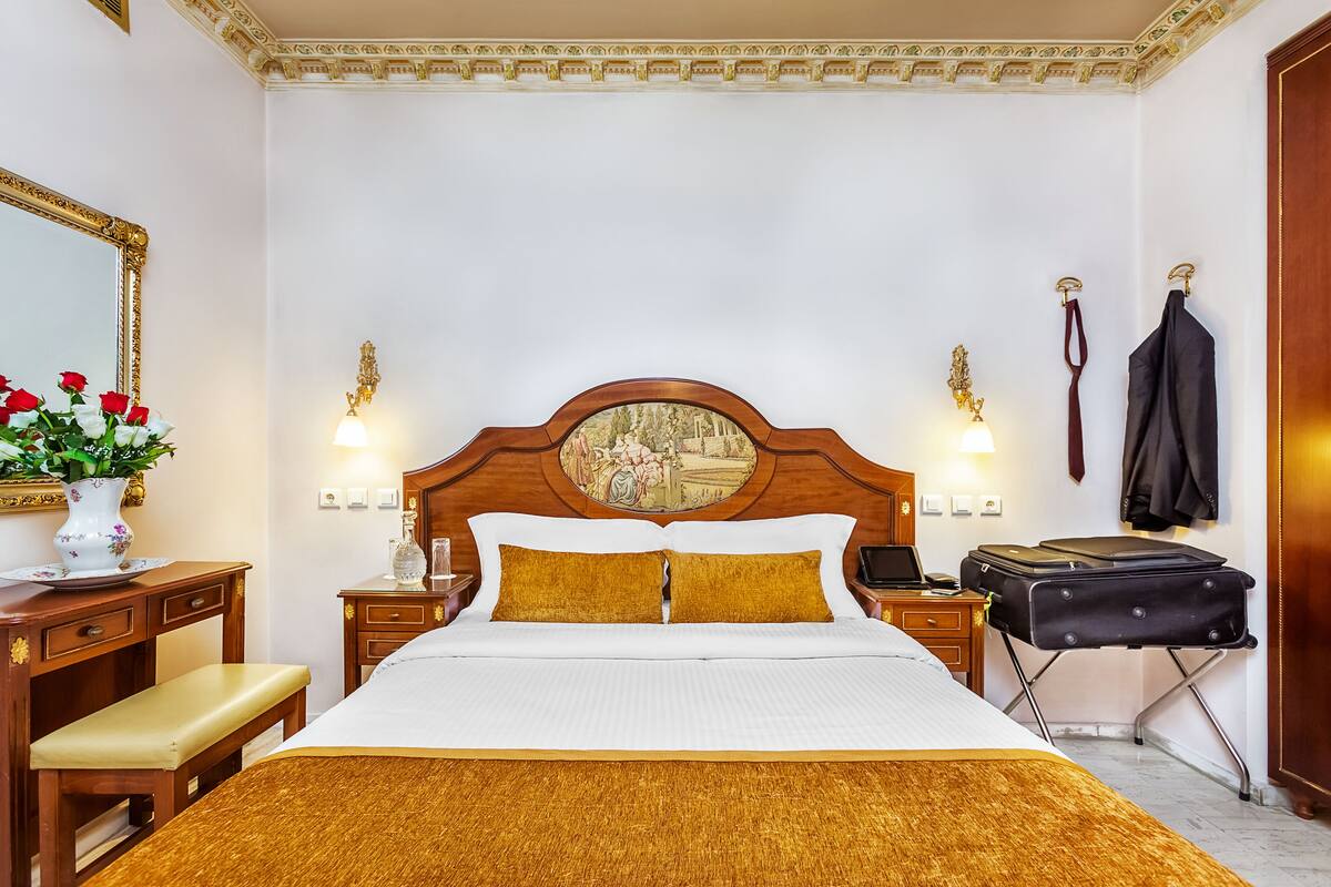 A neatly arranged hotel room with a large bed, bedside tables, a desk, a bench, and a suitcase.