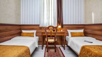 A hotel room with two single beds, a wooden desk with a chair, a lamp, and a patterned rug.