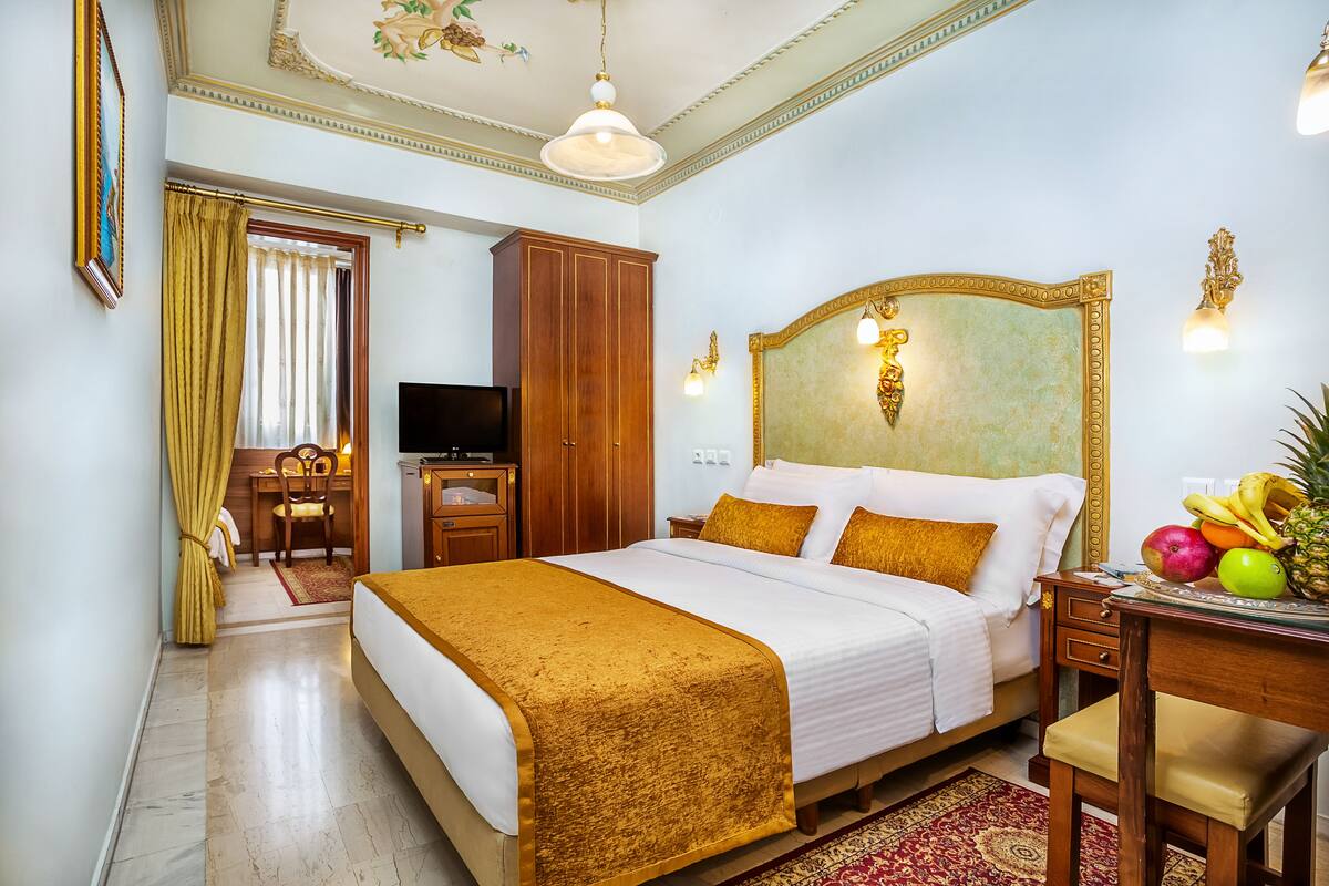 A hotel room with a large bed, a desk with a computer, a television, and a fruit basket on the nightstand.