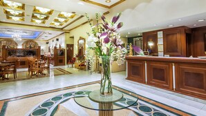 A hotel lobby with a reception desk, dining area, and a large vase of flowers on a glass table. - Imperial Palace Classical Hotel Thessaloniki (Thessaloniki)