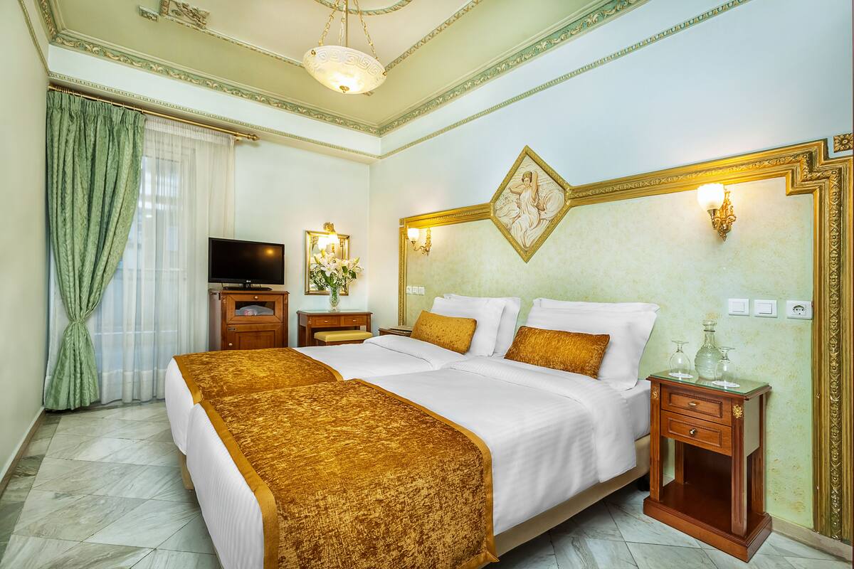 A hotel room with two beds, a television, a nightstand with a lamp, and a decorative wall piece.