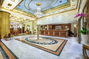 A spacious lobby with a grand chandelier, a reception desk, and a decorative floor design.