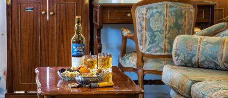 Un mueble de madera con un televisor encima, una mesa con una botella de licor, vasos y un bol de aperitivos.