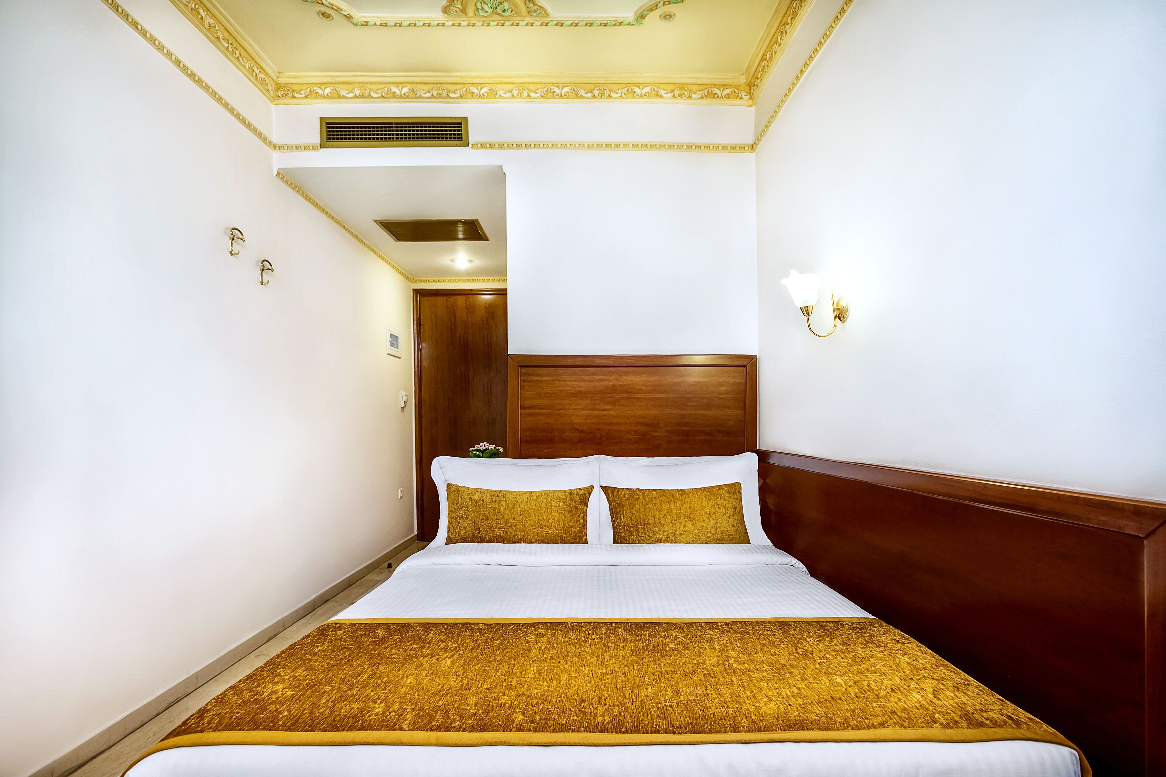Una habitación de hotel con una cama grande, un cabecero de madera y un detalle dorado en la colcha.