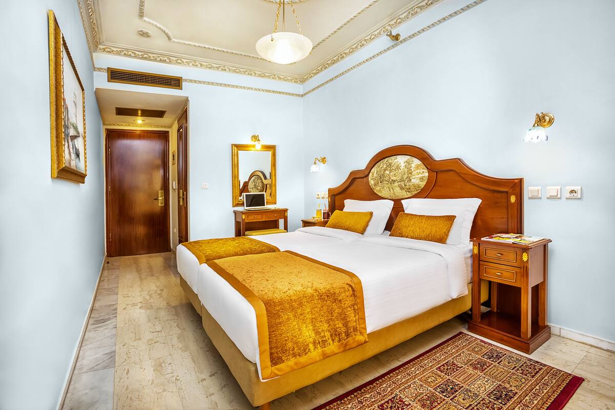 A hotel room with a large bed, a wooden nightstand, a mirror, and a door leading to another room.