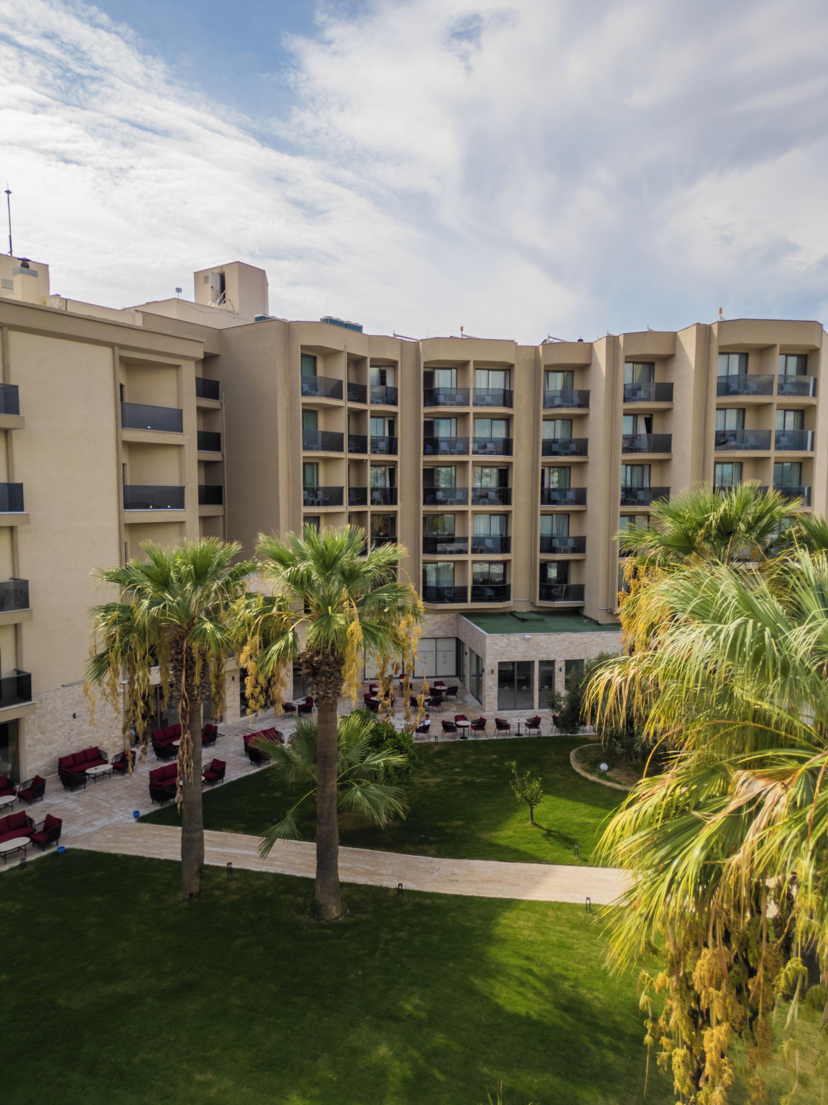 A multi-story hotel with balconies, outdoor seating, and palm trees.