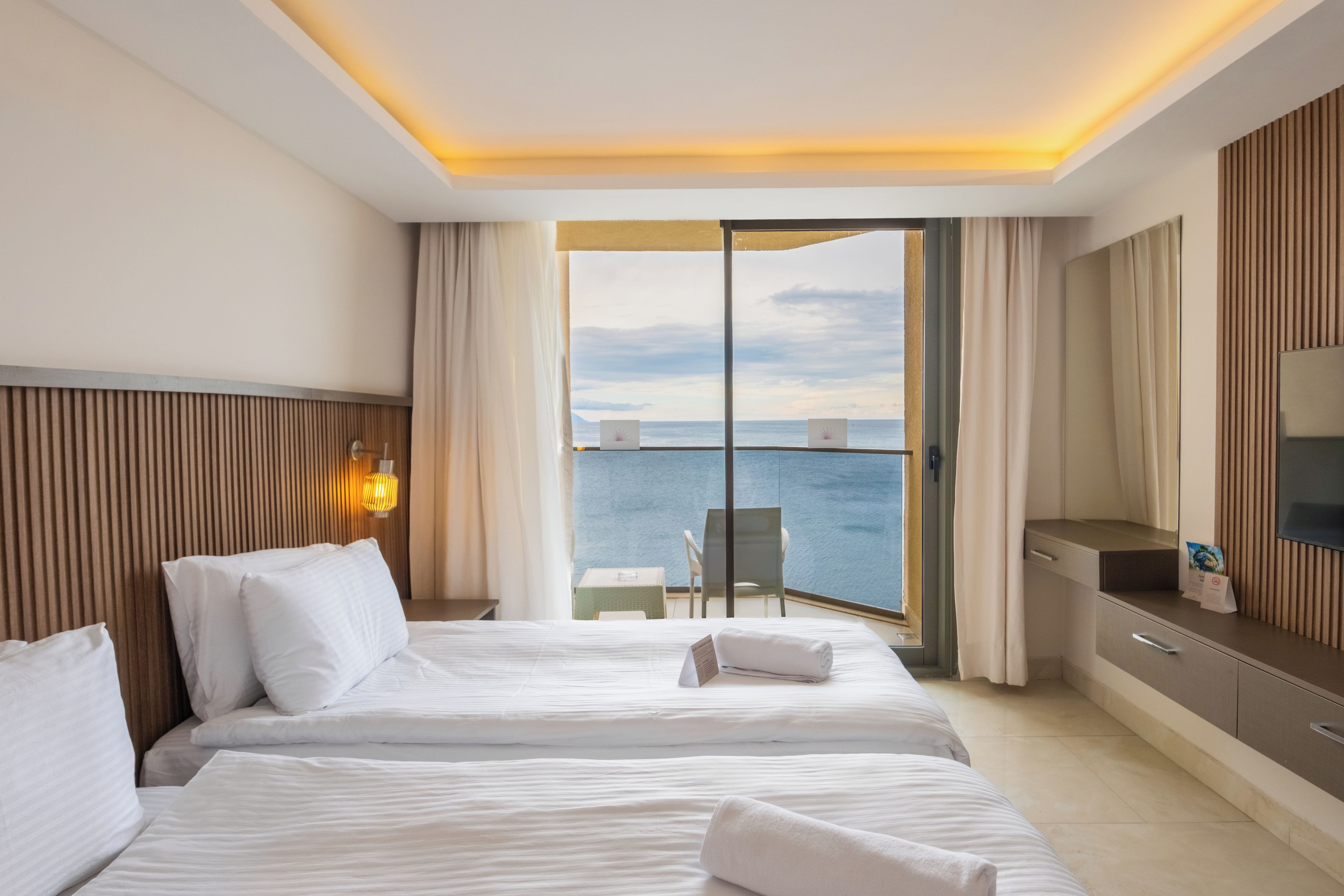 Ett hotellrum med två sängar, ett skrivbord, en stol och utsikt över havet.