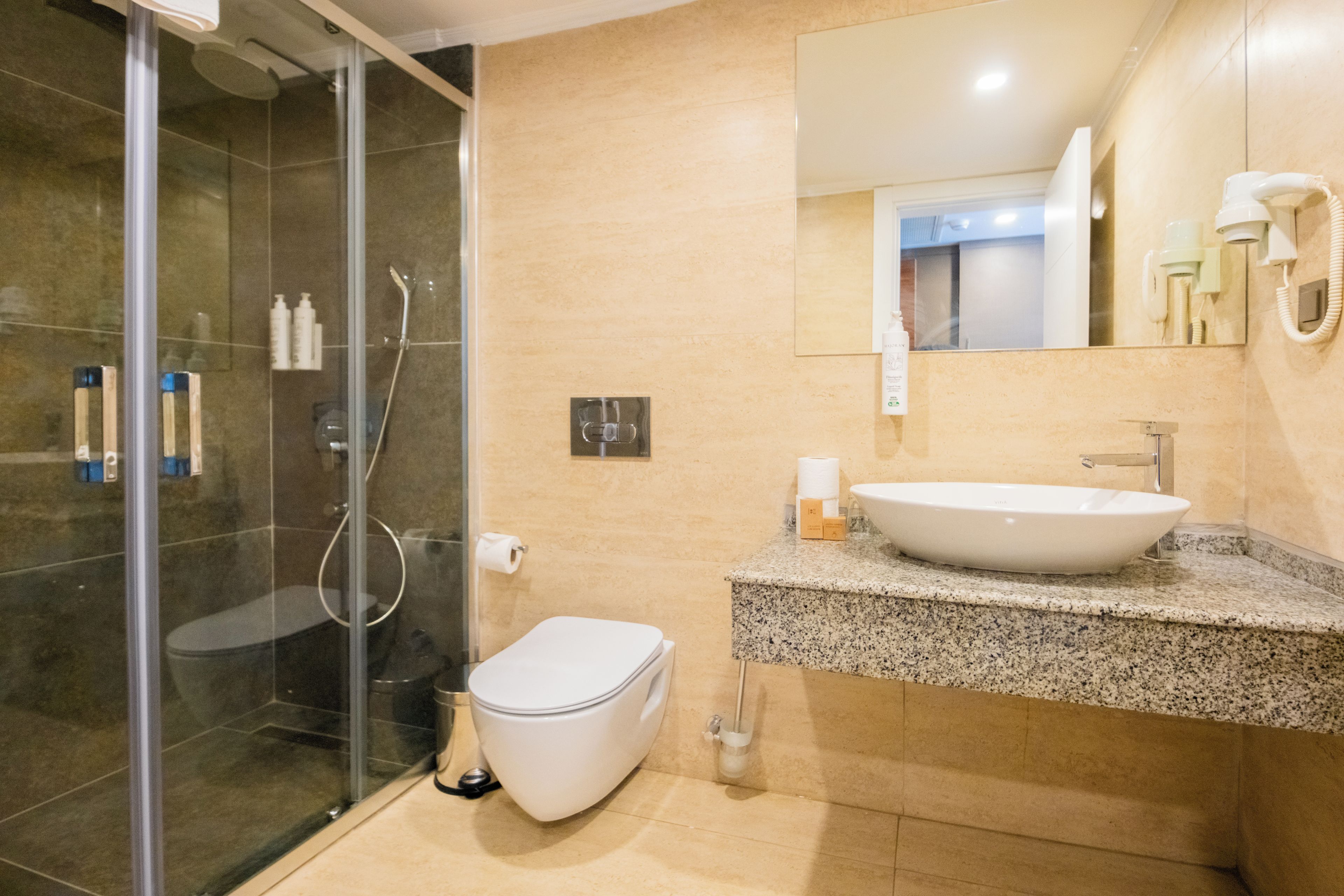 Ein modernes Badezimmer mit einer gläsernen Duschkabine, einer weißen Toilette und einer Waschtischplatte aus Granit.
