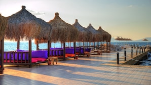 A beachside deck with thatched umbrellas, wooden seating, and a view of the sea.
