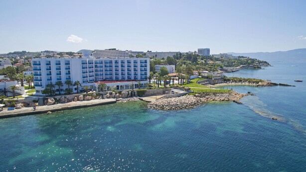 A coastal hotel with a large building, a pool area, and clear blue waters.