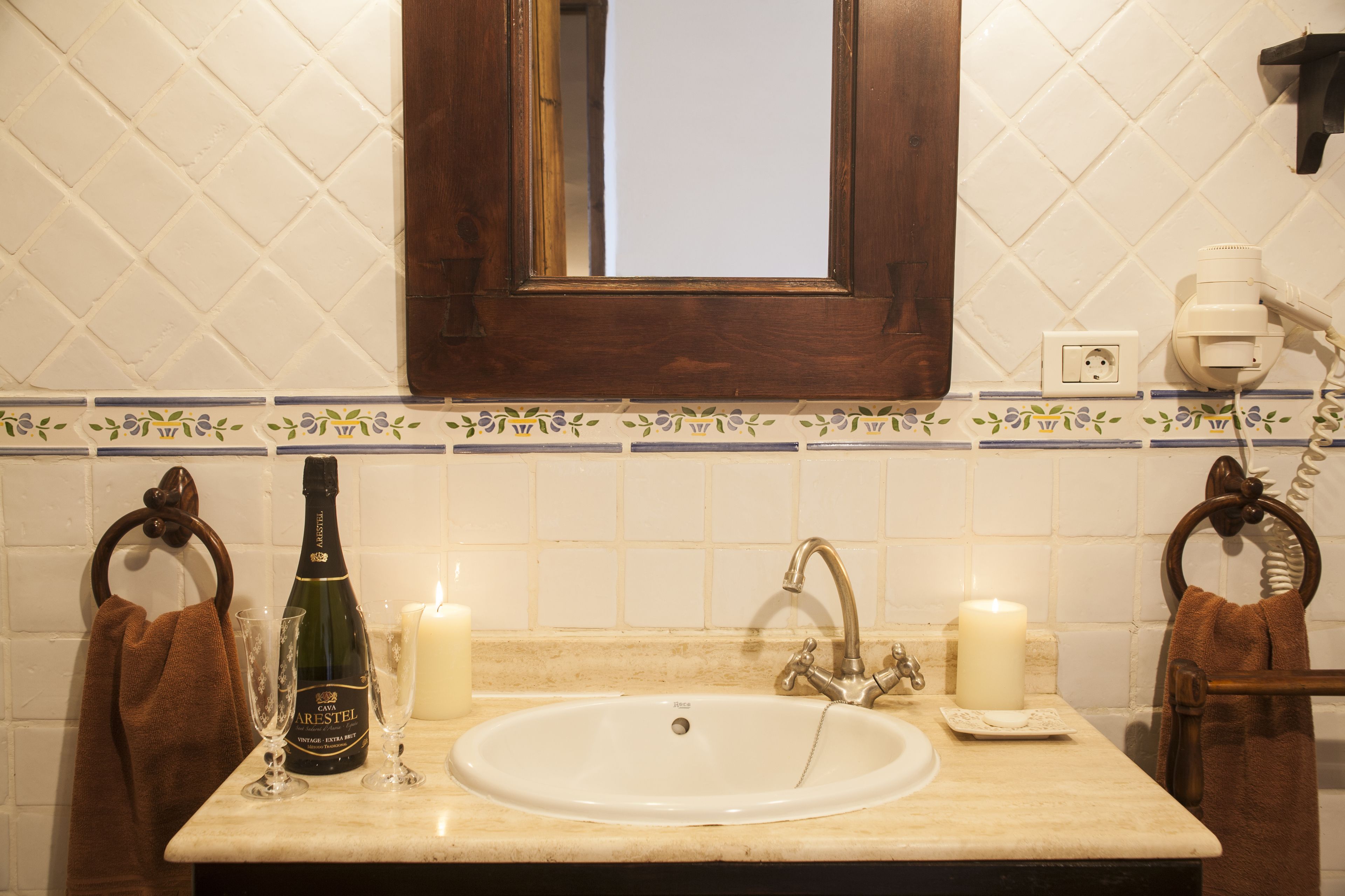 Une salle de bain avec un lavabo, deux serviettes, une bouteille de champagne et deux bougies allumées.
