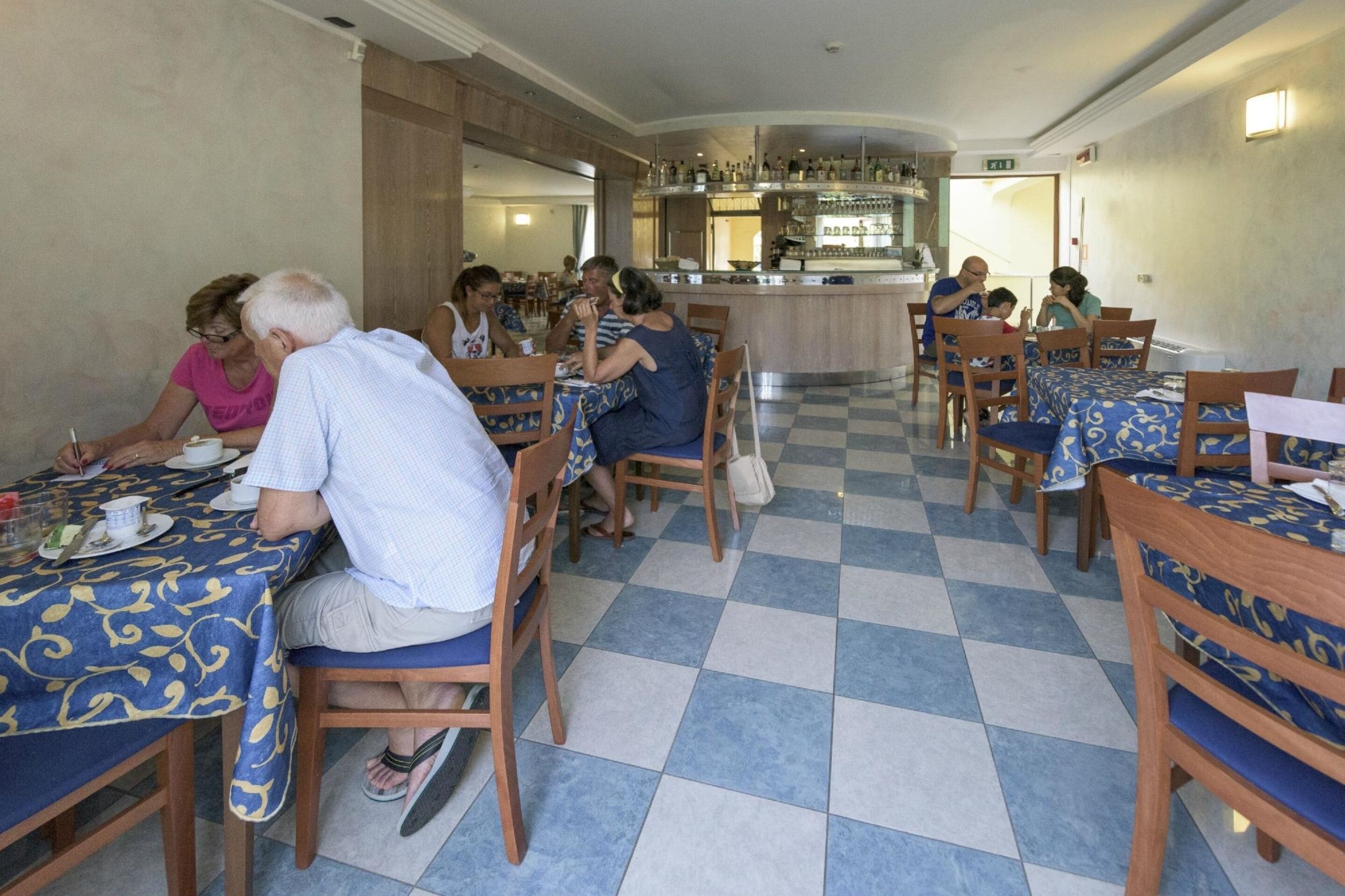 Een restaurant met schakeerd motief tegels, houten tafels met blauwe tafelkleden en een bar op de achtergrond.