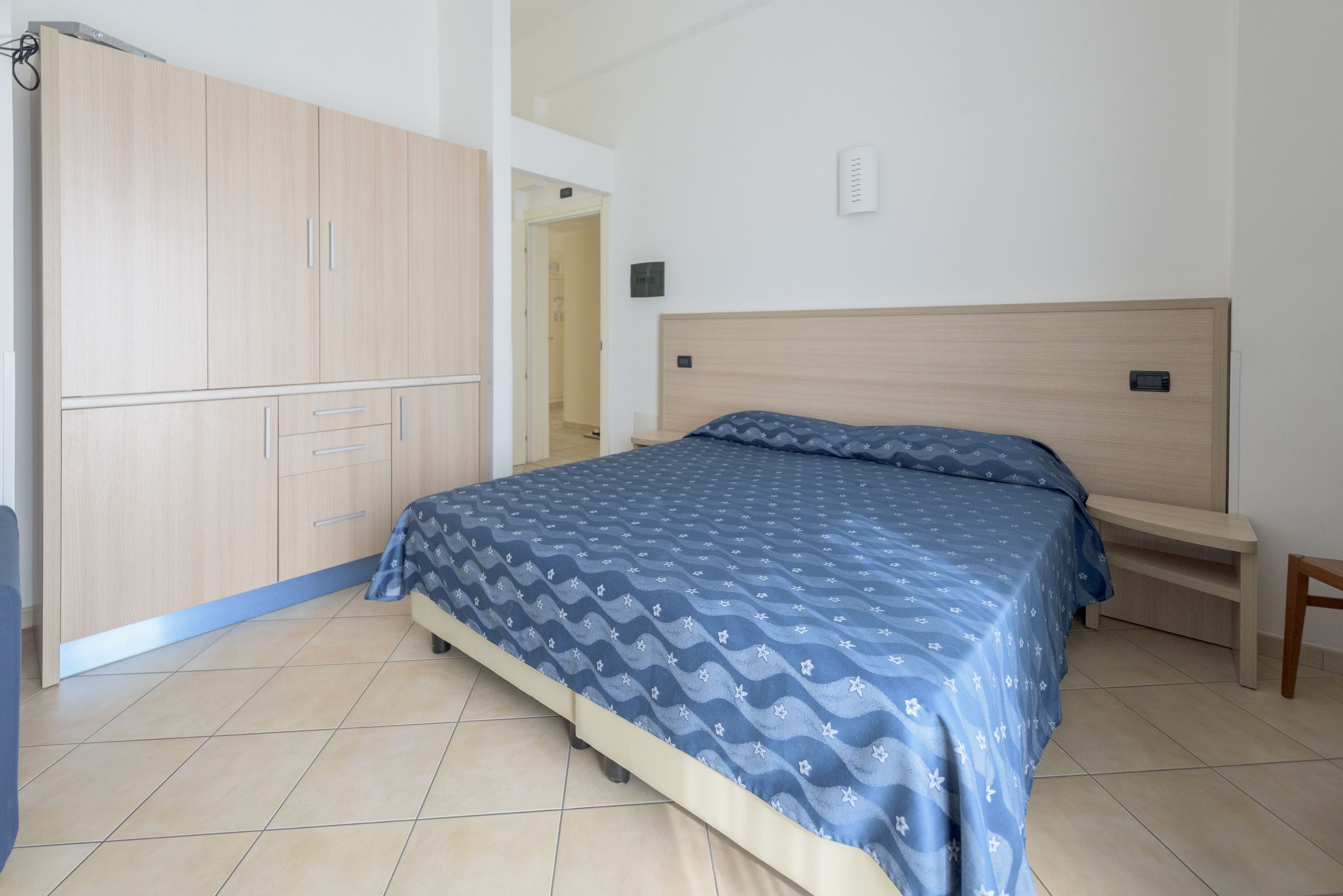 A bedroom with a bed, a wooden wardrobe, and a bedside table.