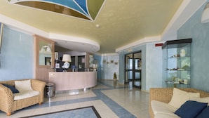 Un vestíbulo con mostrador de recepción, dos sofás de mimbre, piso de baldosas y una vitrina de cristal con objetos decorativos.