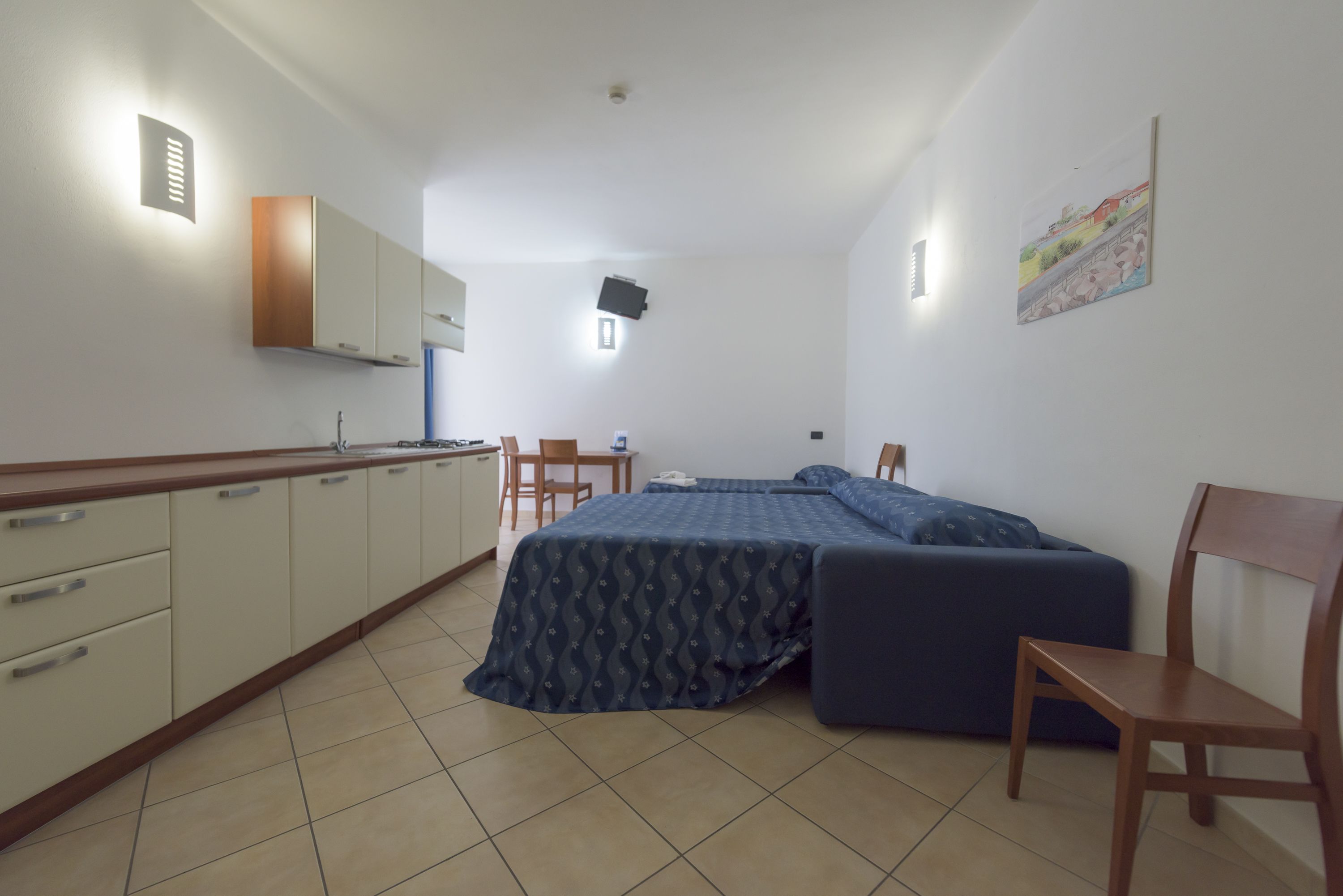 A compact room with a kitchenette, a bed with a patterned bedspread, and a chair.