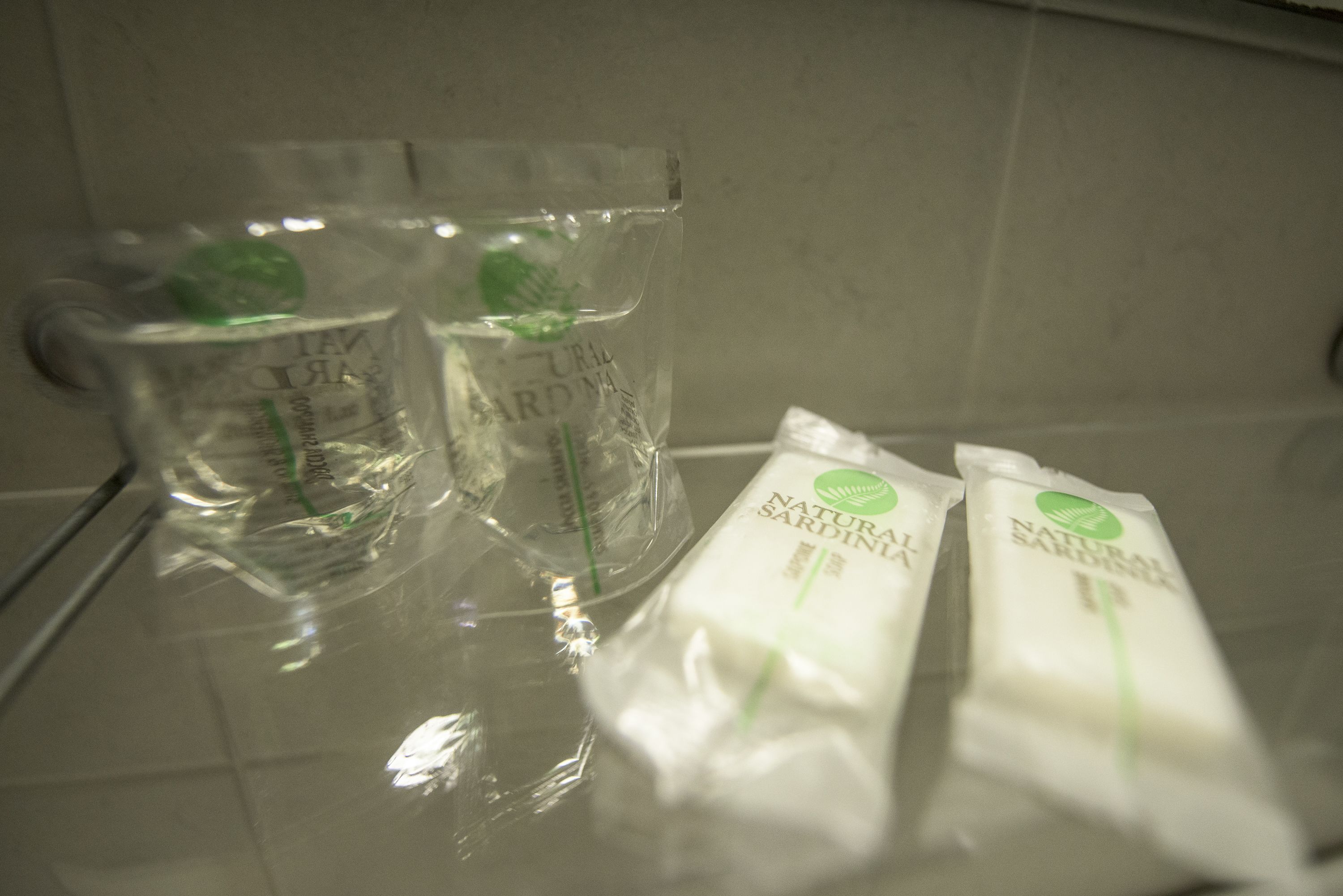 Zwei klare Gläser und zwei Packungen natürliches Sardellenöl auf einer spiegelnden Oberfläche.