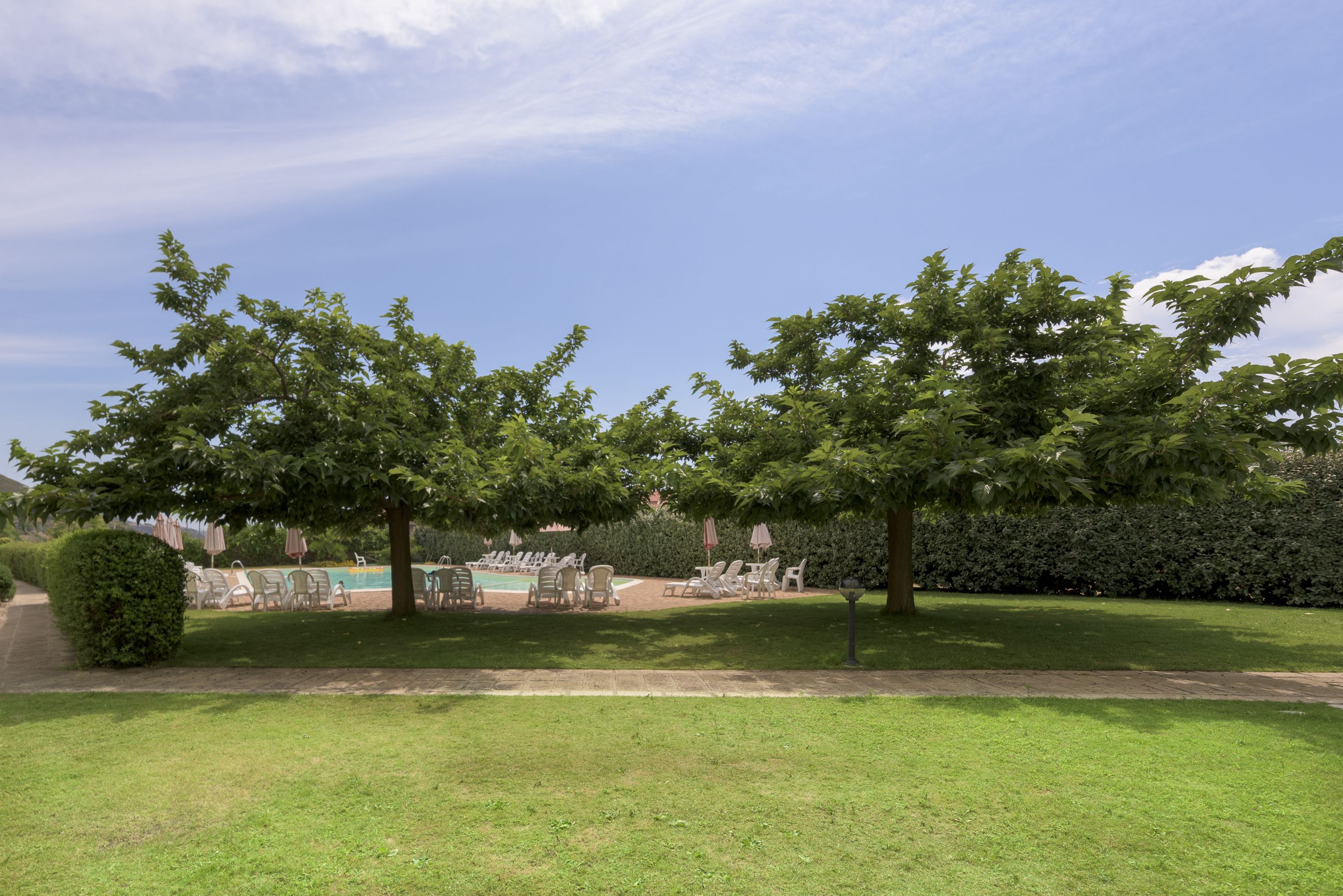 A well-maintained garden with a swimming pool, lounge chairs, and a clear sky.