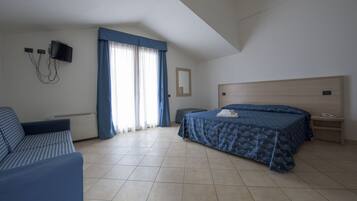 Une chambre à coucher avec un lit, un canapé, un téléviseur fixé au mur et une fenêtre avec des rideaux.