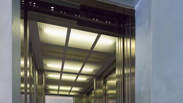 An elevator with a potted plant, metallic walls, and a tiled floor.