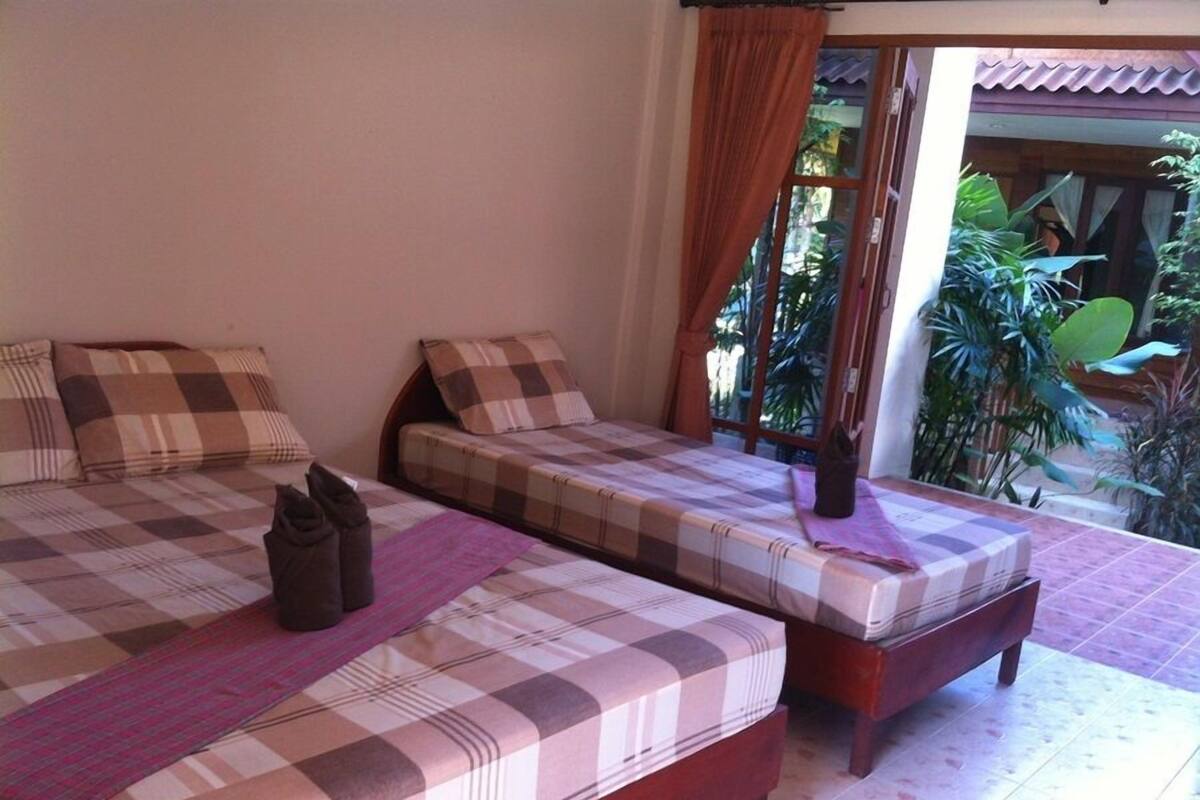 Habitación con dos camas, cada una con colcha y almohadas a cuadros. Hay una ventana con cortinas y vistas al exterior de follaje.