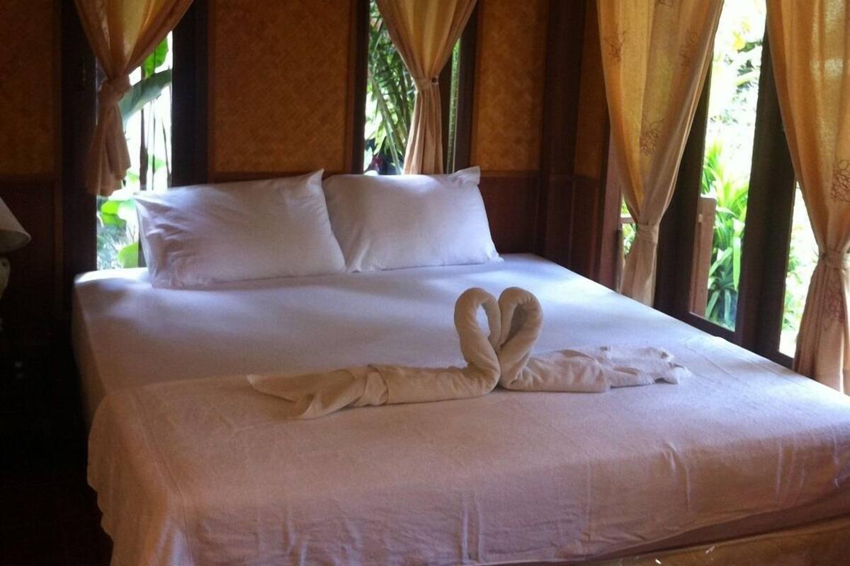 Una cama grande con sábanas blancas, dos almohadas y una disposición de toallas en forma de corazón.