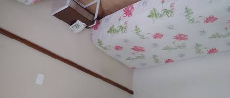 A corner of a room with a floral-patterned ceiling, a wooden beam, and a small white shelf.