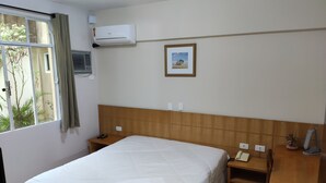 A hotel room with a bed, bedside tables, a telephone, an air conditioning unit, a window with curtains, and a framed picture on the wall. - Hara Palace Hotel (Curitiba)