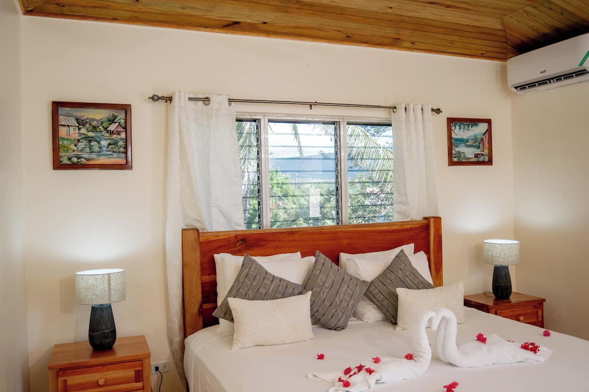A neatly made bed with a wooden headboard, white bedding, and decorative pillows. There are two bedside tables with lamps, and a window with curtains.