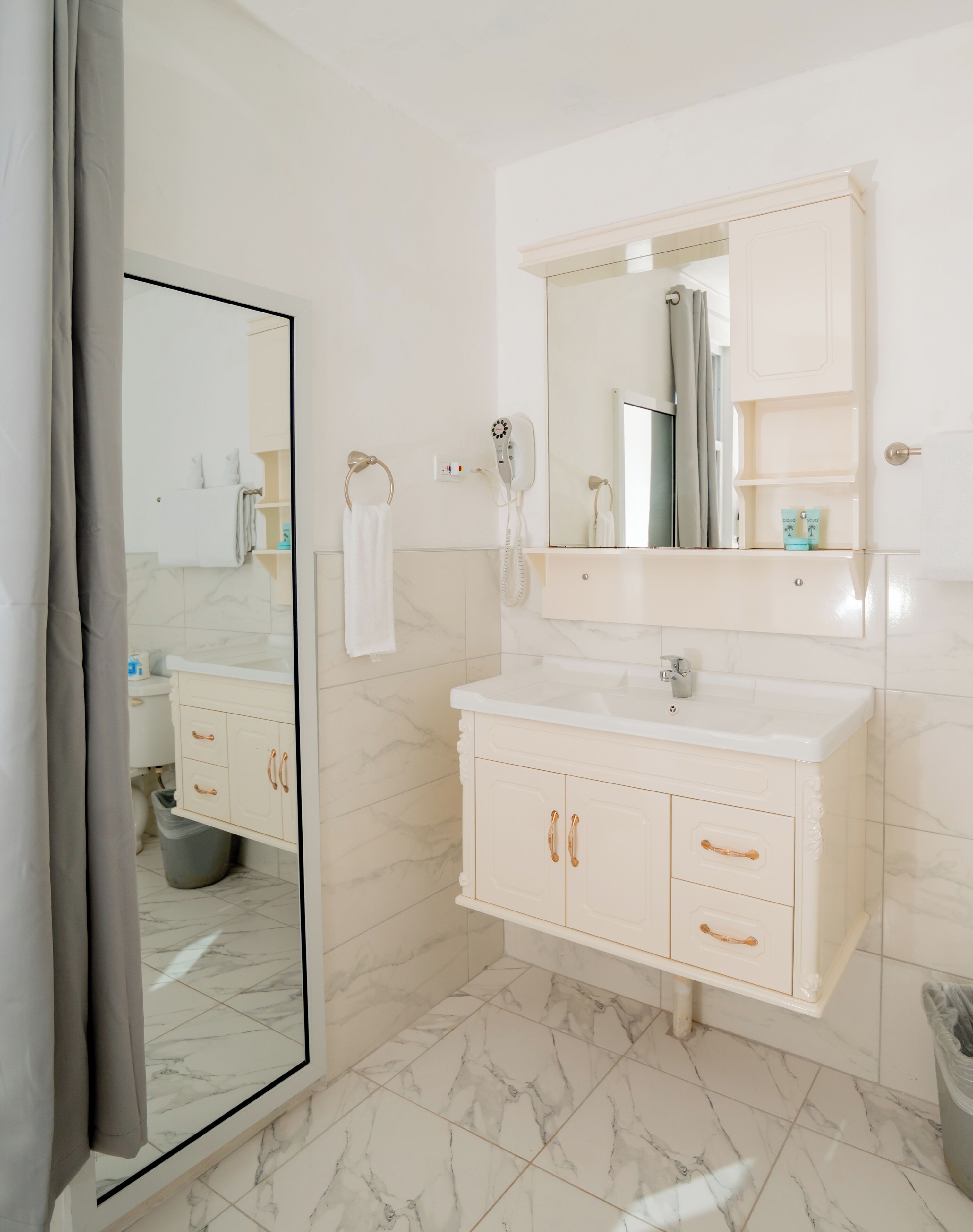 A modern bathroom with a white vanity, a large mirror, and a hairdryer on the wall.